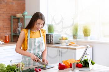 Beautiful woman preparing tasty vegetable salad in kitchen at home�