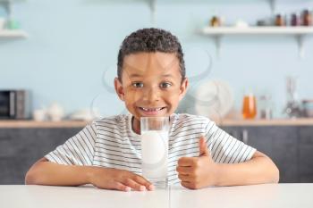 Cute African-American boy with glass of milk showing thumb-up at table�