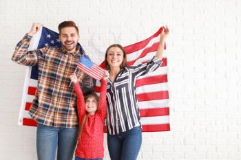 Happy young family with national flags of USA near white brick wall�