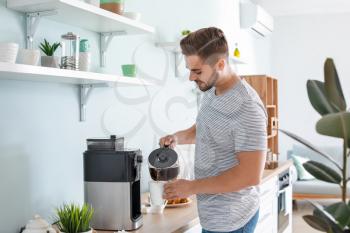 Handsome man using coffee machine in kitchen�