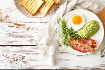Plate with tasty fried egg, avocado and bacon on wooden table�