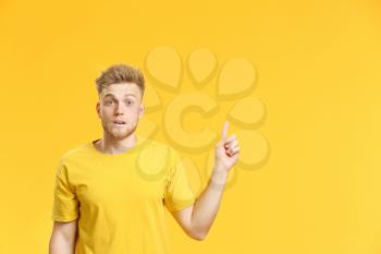 Portrait of scared young man pointing at something on color background�