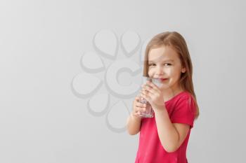 Cute little girl drinking water on light background�