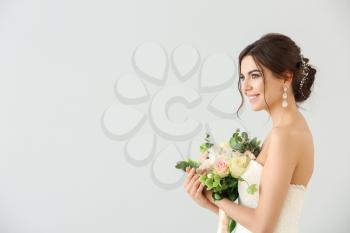 Beautiful young bride with bouquet of flowers on light background�