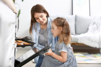 Young woman and her little daughter baking tasty cookies at home�