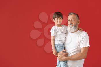 Cute little boy with grandfather on color background�