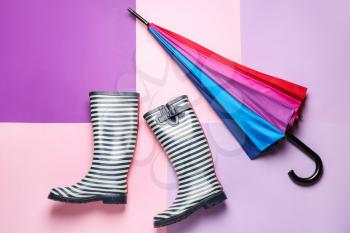 Stylish umbrella and gumboots on color background�