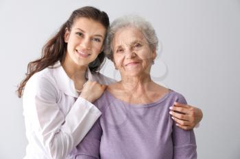 Young doctor with senior woman on grey background�