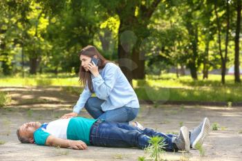 Female passer-by calling an ambulance for unconscious mature man outdoors�
