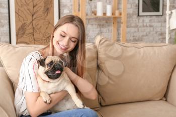Beautiful young woman with cute pug dog sitting on sofa at home�
