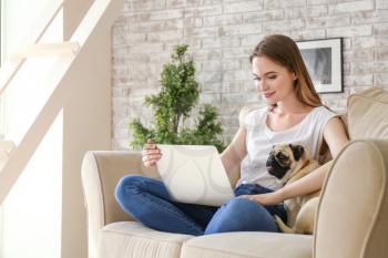 Beautiful young woman with cute pug dog working on laptop at home�