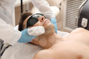 Handsome man undergoing procedure of laser hair removing in beauty salon�