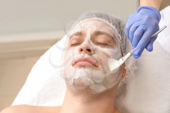 Handsome man undergoing treatment with facial mask in beauty salon�