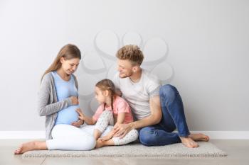 Beautiful pregnant woman with her family sitting near light wall�