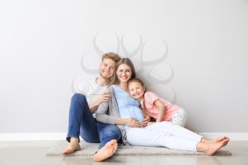 Beautiful pregnant woman with her family sitting near light wall�
