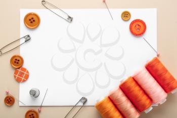 Set of sewing threads with accessories and sheet of paper on color background�