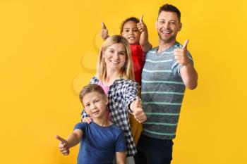 Happy couple with little adopted children showing thumb-up on color background�