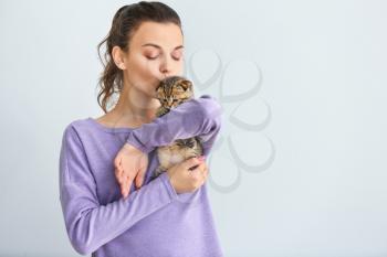 Beautiful young woman with cute little kitten on light background�