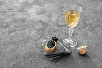 Bread with delicious caviar and glass of champagne on grunge background�