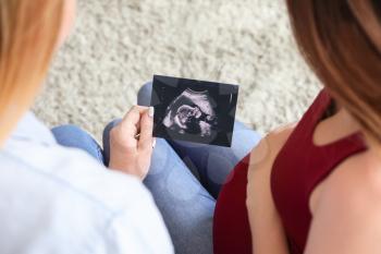 Pregnant lesbian couple with sonogram image at home�