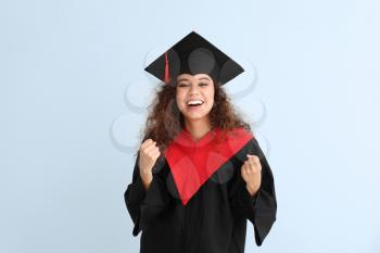 Happy African-American student in bachelor robe on color background�