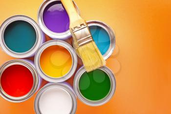 Cans of paints and brush on color background�