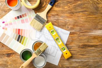 Cans of paint with supplies, palette samples and house plan on wooden table�