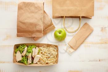 Paper box and bags with delicious food on white wooden background�