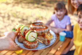 Man with tasty grilled meat on plate for his family outdoors, closeup�