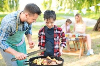Little boy with father cooking tasty food on barbecue grill outdoors�