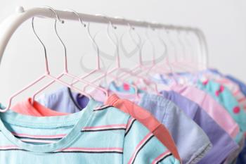 Stylish kid clothes hanging on rack against light background, closeup�