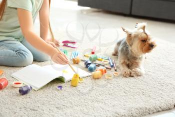 Cute little girl with dog painting while sitting on carpet�