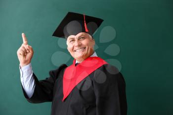 Mature man in bachelor robe and with raised index finger on color background�