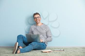Male blogger with laptop sitting near color wall�