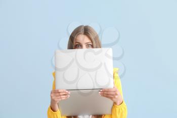 Surprised young woman with laptop on color background�