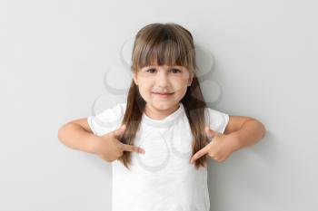 Little girl pointing at her t-shirt on light background�