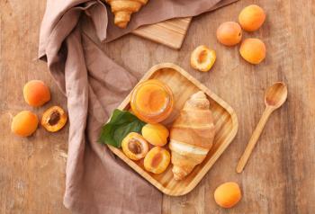 Plate with tasty apricot jam and croissant on wooden table�
