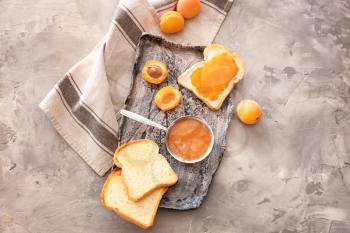 Plate with tasty apricot jam and bread slices on grunge background�
