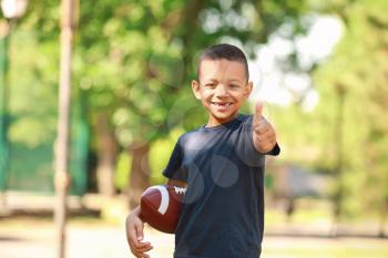 Cute little African-American boy with rugby ball showing thumb-up gesture in park�
