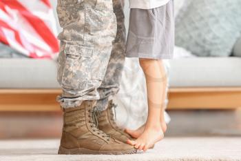 Boy standing on feet of his military father at home�