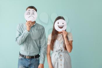 Couple hiding faces behind sheets of paper with drawn emoticons on color background�