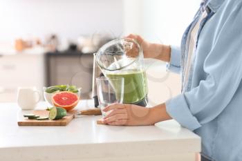 Woman pouring tasty smoothie from blender into glass in kitchen�