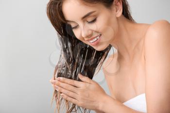 Beautiful young woman washing hair against grey background�