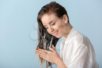Beautiful young woman applying mousse on her hair after washing against color background�