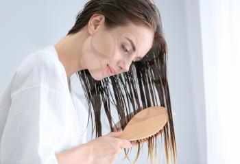 Beautiful young woman brushing hair after washing at home�