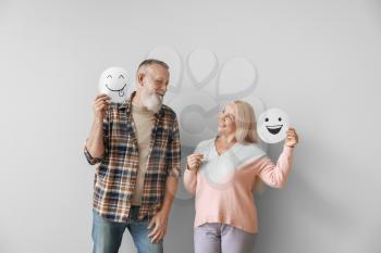 Happy mature couple with emoticons against light background�