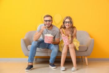 Young couple with popcorn watching movie on sofa near color wall�
