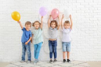 Cute little children with air balloons near white brick wall�