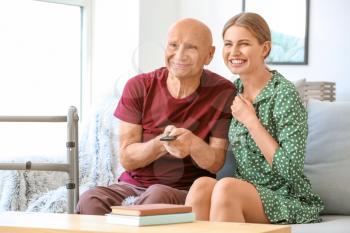 Young woman and her elderly father watching TV in nursing home�