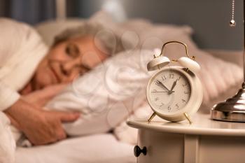 Alarm clock on table of sleeping senior woman at night�